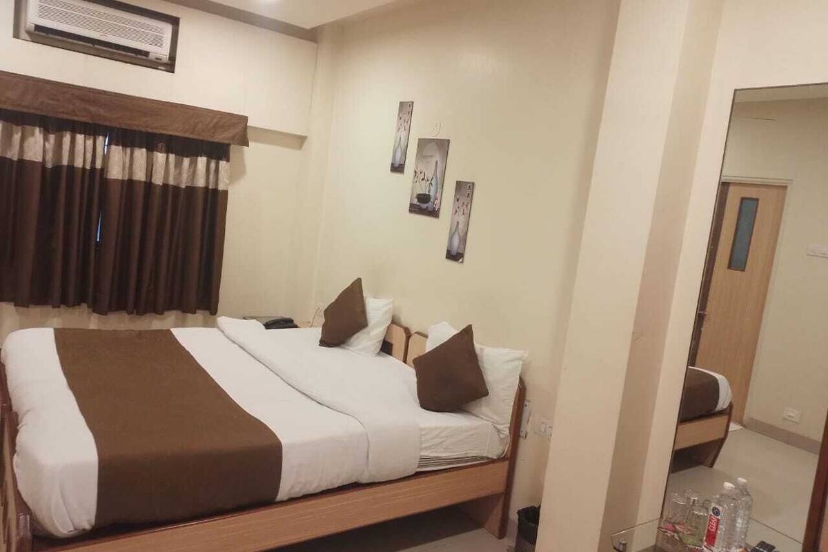 Un cuarto de hotel con una cama grande, una mesita de noche con una botella y un espejo en la pared.