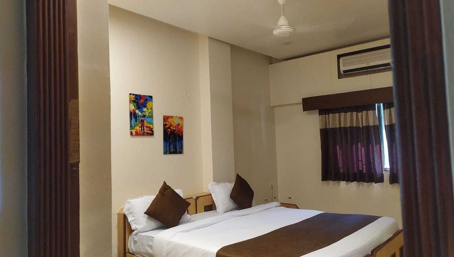A bedroom with a bed, two pillows, a window with curtains, and two paintings on the wall.