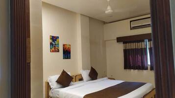 A bedroom with a bed, two pillows, a window with curtains, and two paintings on the wall.