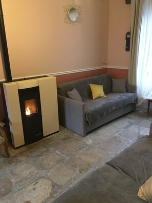 Ein Wohnzimmer mit Steinboden, einem grauen Sofa mit Kissen und einem weißen Heizgerät sowie einem an der Wand befestigten Spiegel.