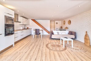 Eine moderne Küche mit weißen Schränken und einem eingebauten Ofen. Eine Holztreppe führt zu einem Wohnbereich mit einer Couch und einem Couchtisch.