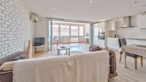 A modern apartment with a white brick wall, a dining area, a kitchen, and a living room with a sofa and a TV. - Duplex 2 bedrooms Terrace Sea view A2B024 (Cannes)