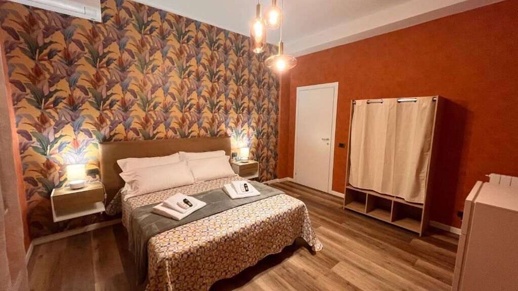 A bedroom with a bed, bedside lamps, a wardrobe, and a floral wallpaper.