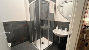 Ein modernes Badezimmer mit einer Duschkabine, einem Waschbecken mit Spiegel und dunkel gefliesten Wänden.