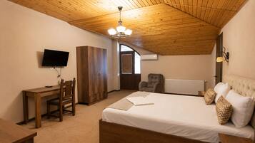 Quarto com teto de madeira, uma cama, escrivaninha com cadeira, televisão e guarda-roupa.