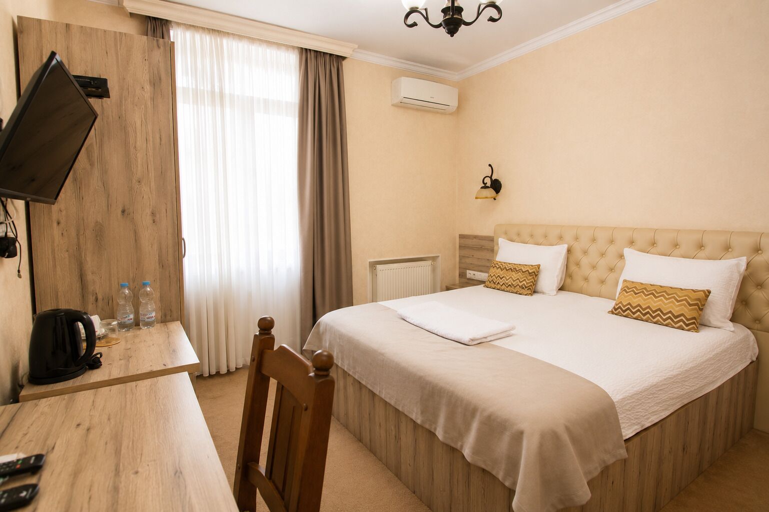 Habitación de hotel con cama, escritorio, silla, televisor y ventana con cortinas.