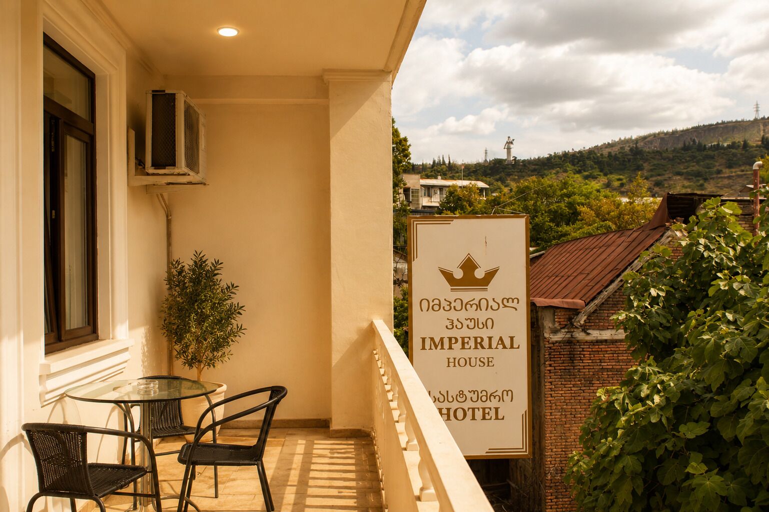 Un balcón con una mesa, sillas, una planta en maceta y un cartel del Hotel Imperial House.