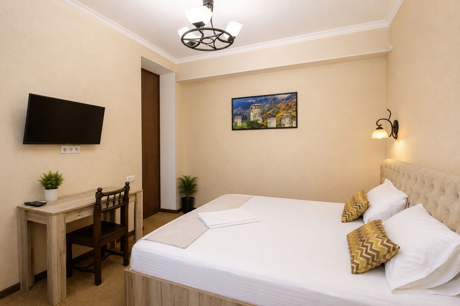 A hotel room with a bed, a desk, a chair, a television, and a painting on the wall.
