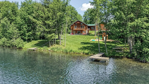 A cabin by a lake with a dock, surrounded by trees and a well-maintained lawn.