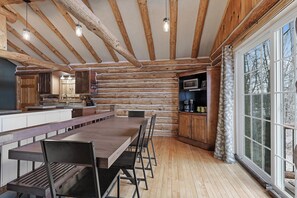 Interior rústico de cabana com mesa de jantar de madeira, bancos e área de cozinha com armários de madeira e micro-ondas.