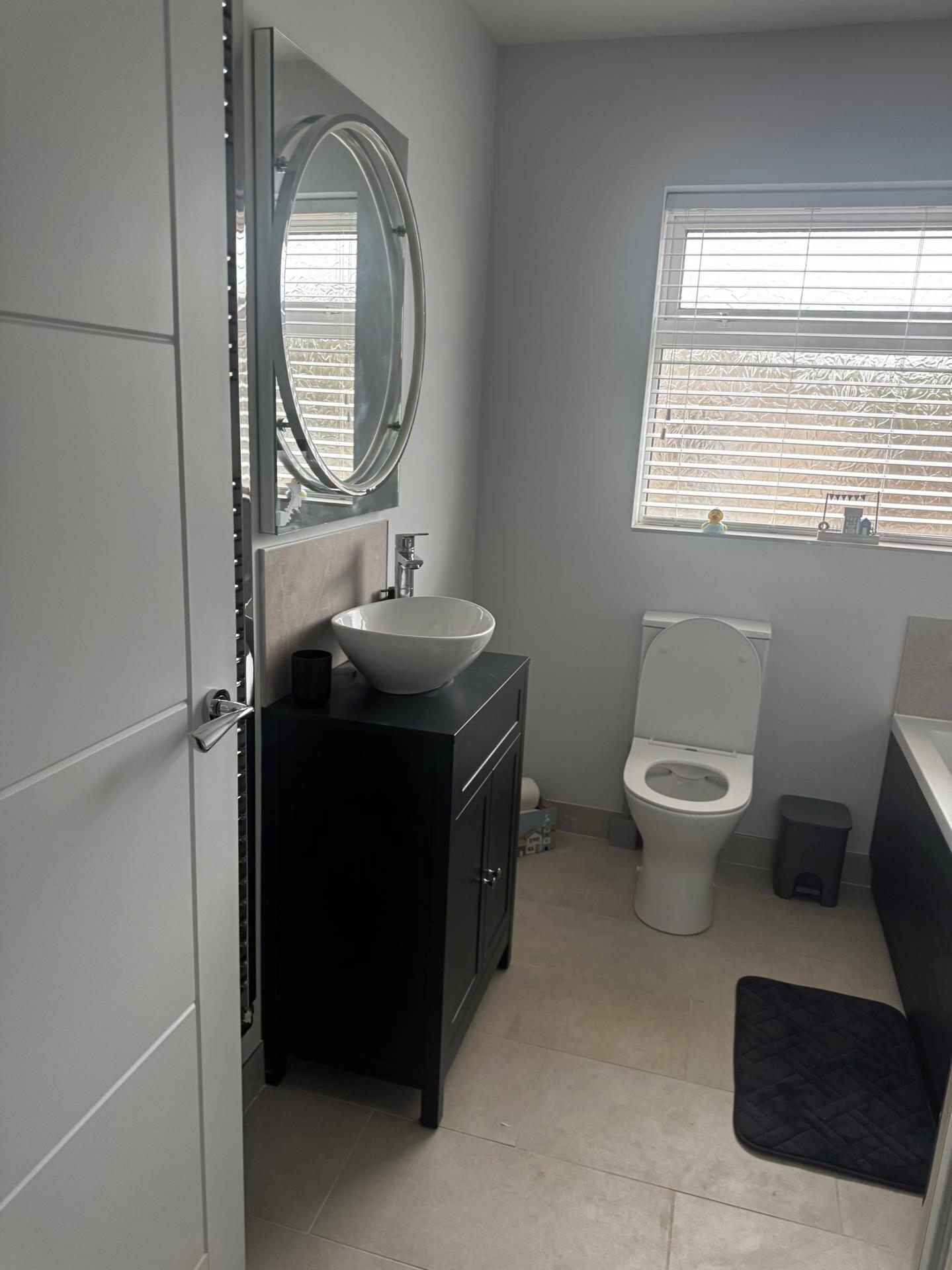 A compact bathroom with a white sink, a toilet, and a window with blinds.