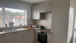 A modern kitchen with white cabinets, a built-in oven, and a window with blinds. - 3 Bed Cottage - Sleeps 5 - Pets - Hottub - Garden (King's Lynn)