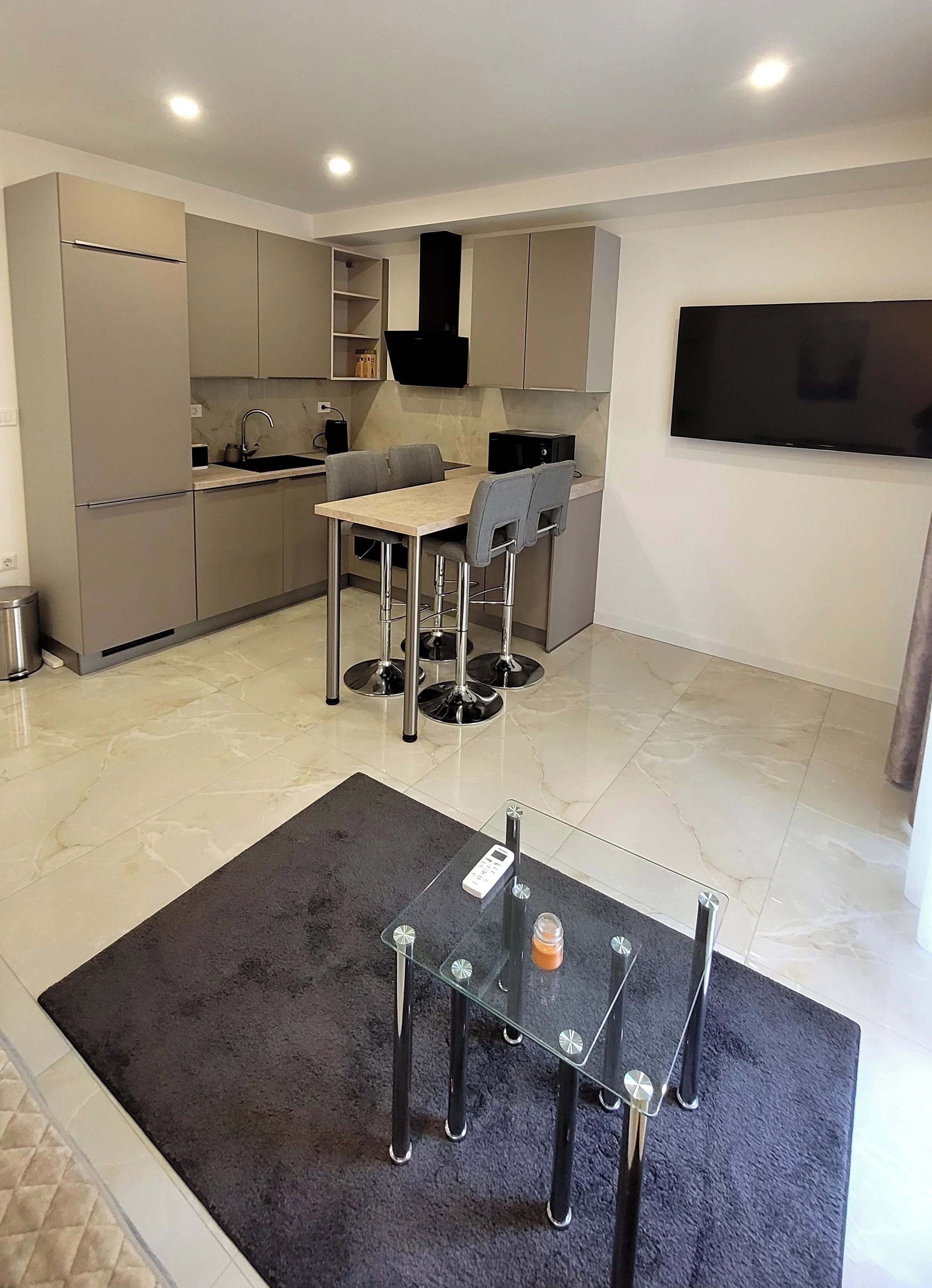 Une cuisine moderne avec un coin repas, un téléviseur fixé au mur et une petite table avec un plateau en verre.