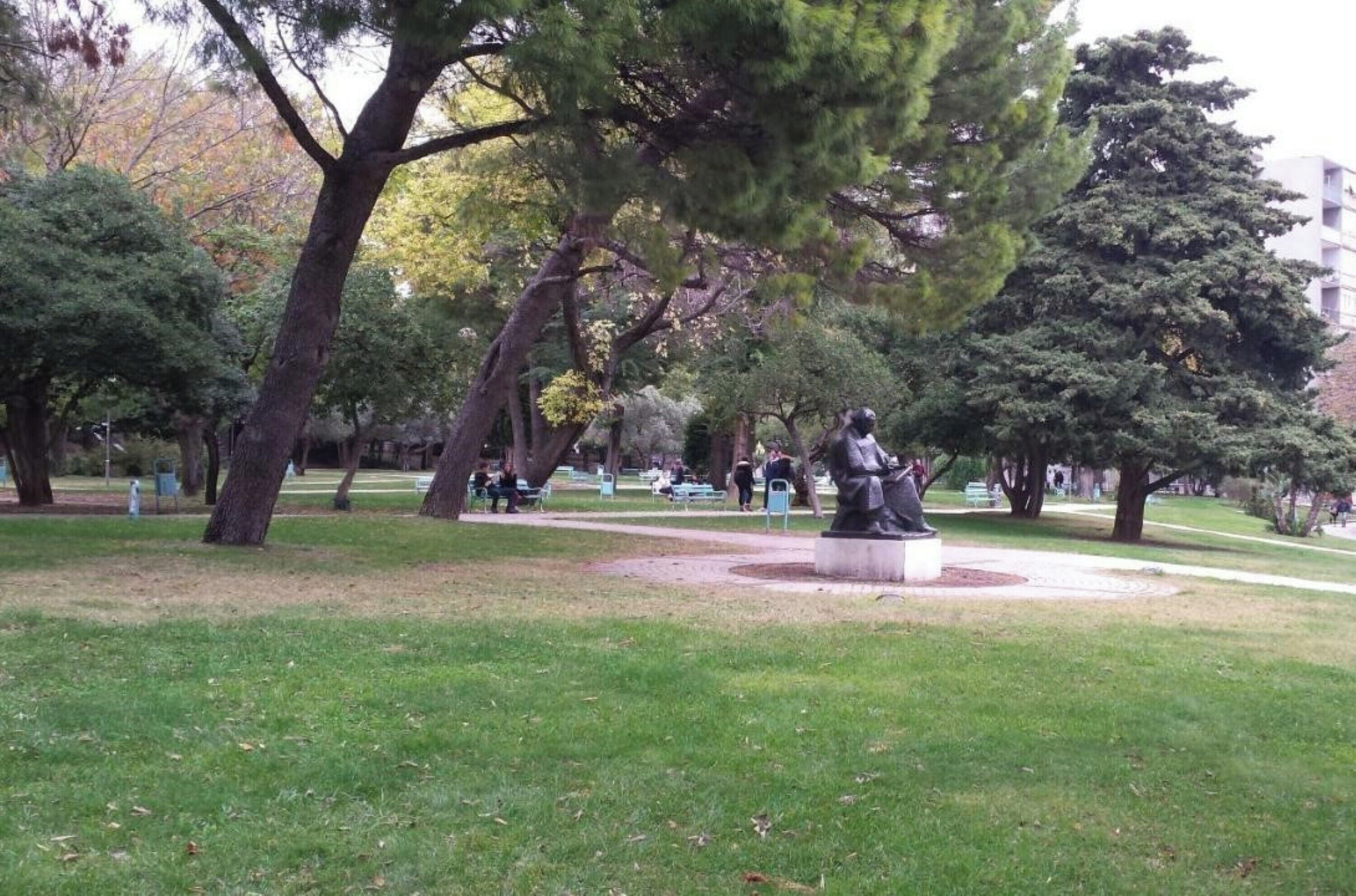 A park with a statue, benches, and trees.