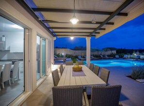 An outdoor dining area with a pool, wicker furniture, and a view of the pool at dusk.