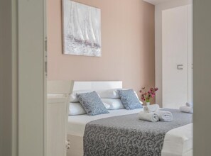 A bedroom with a bed, pillows, a painting, a vase with flowers, and towels.
