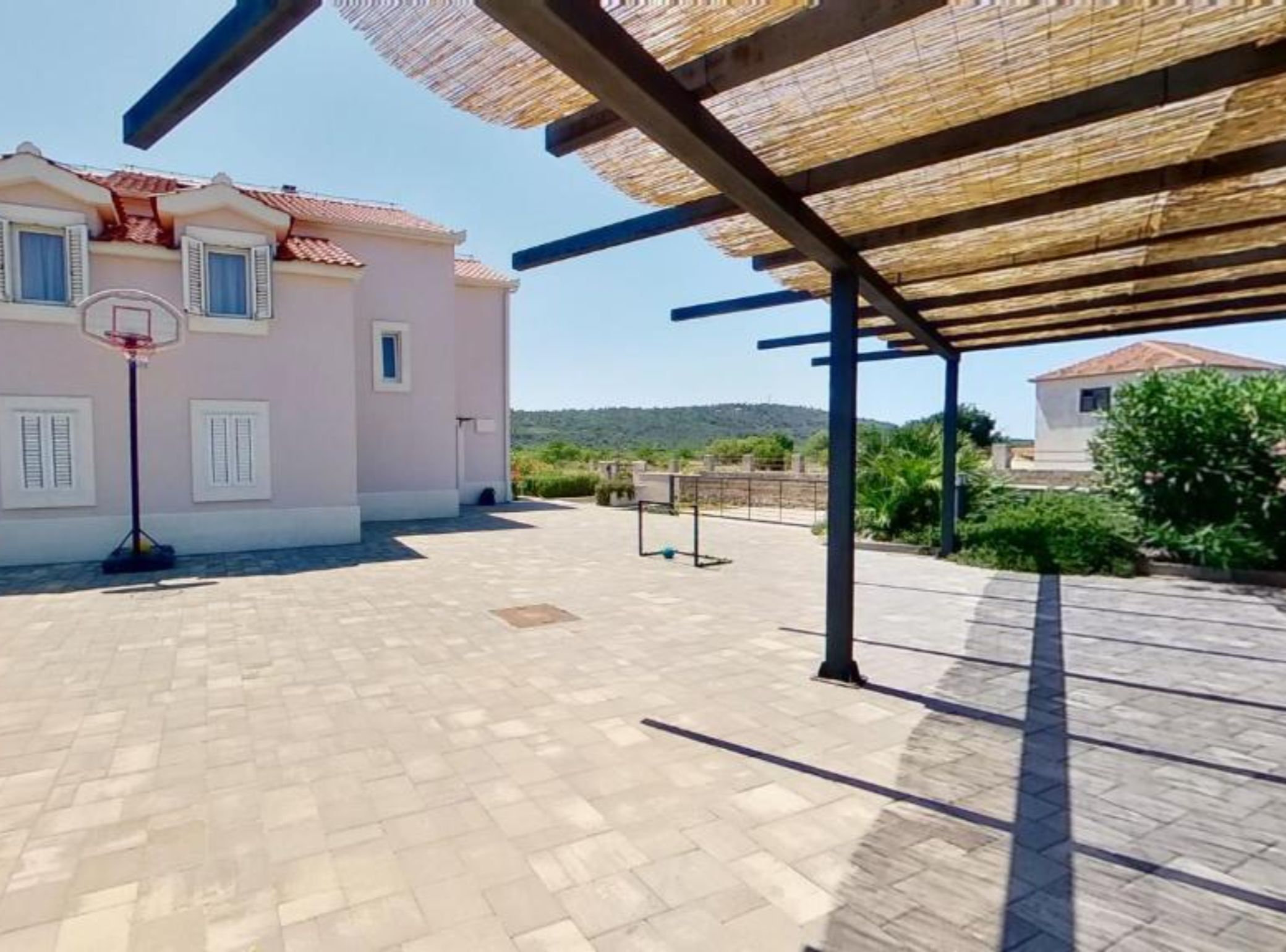 Un espacio exterior cubierto con canasta de baloncesto, una pérgola y un edificio con techo de tejas.