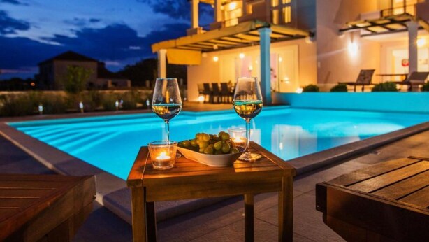 A poolside setting with two glasses of wine, a bowl of grapes, and a candle on a wooden table. - Adriatic Pearl (Solta)