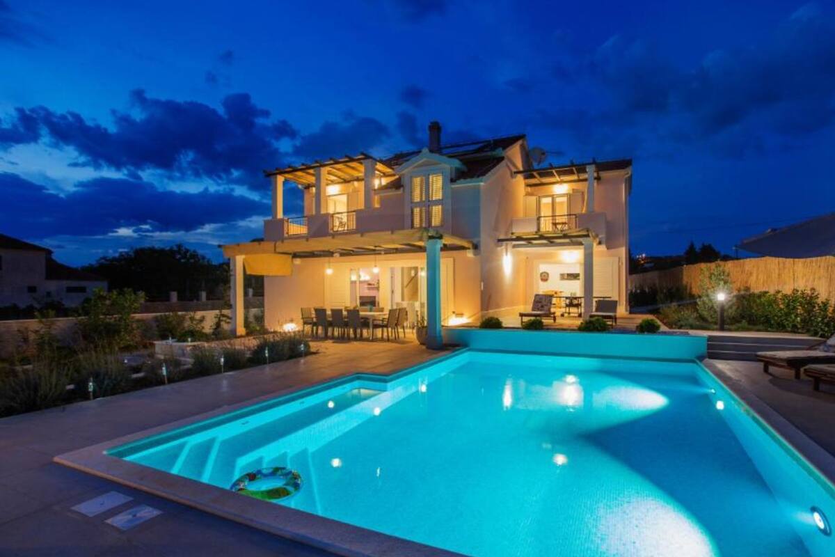 A two-story house with a swimming pool, outdoor seating, and a well-lit patio area.