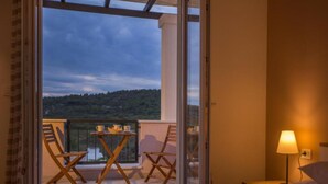 A bedroom with a bed, a nightstand, a lamp, and a view of a balcony with a table and chairs. - Adriatic Pearl (Solta)