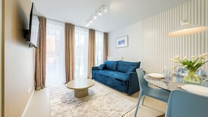 A modern living room with a blue sofa, a round coffee table, and a dining table set for two. - Apartamenty Sun & Snow West Park (Kołobrzeg)