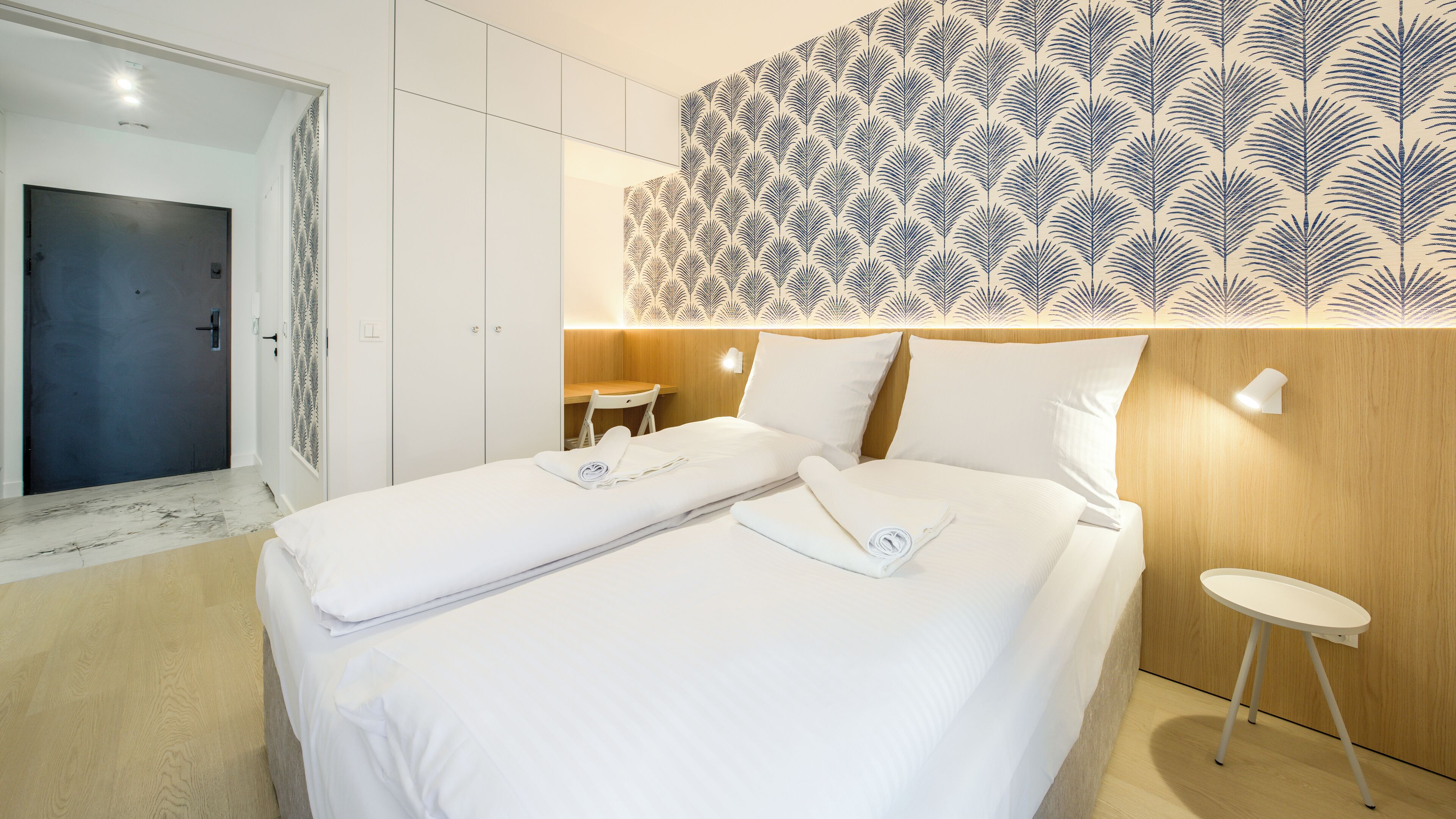 Ein Hotelzimmer mit Bett, einem kleinen Tisch und einer Wand mit Blattmuster.