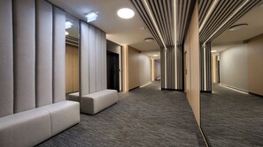 Un couloir d’hôtel moderne, doté d’un sol recouvert de moquette, de bancs intégrés et d’un plafond à motifs rayés.