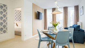 A modern hotel room with a dining area, a TV mounted on the wall, and a large window with curtains. - Apartamenty Sun & Snow West Park (Kołobrzeg)