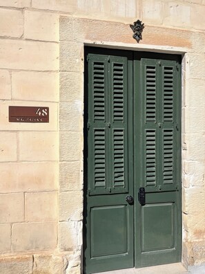 Eine grüne Tür mit Fensterläden, eine Messingschild mit der Nummer 48 und ein kleines dekoratives Element darüber.