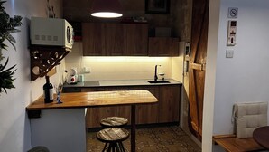 Ett kompakt kök med träskåp, en inbyggd mikrovågsugn, en diskho och en liten matplats med barstolar.