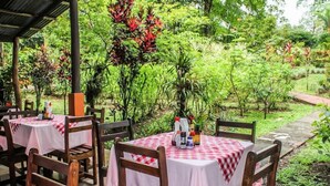 An outdoor restaurant with tables covered in checkered tablecloths, surrounded by lush greenery and plants. - Cabinas Faro Arenal (La Fortuna)