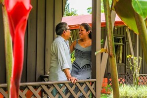 A wooden structure with a balcony, surrounded by greenery and a red roof. - Cabinas Faro Arenal (La Fortuna)