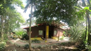 A small, single-story wooden house with a porch, surrounded by dense tropical vegetation. - Cabinas Faro Arenal (La Fortuna)