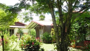 A garden with a house, a pathway, and various plants. - Cabinas Faro Arenal (La Fortuna)