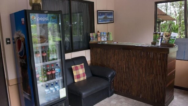 A reception area with a Pepsi refrigerator, a black leather sofa, and a wooden reception desk. - Cabinas Faro Arenal (La Fortuna)