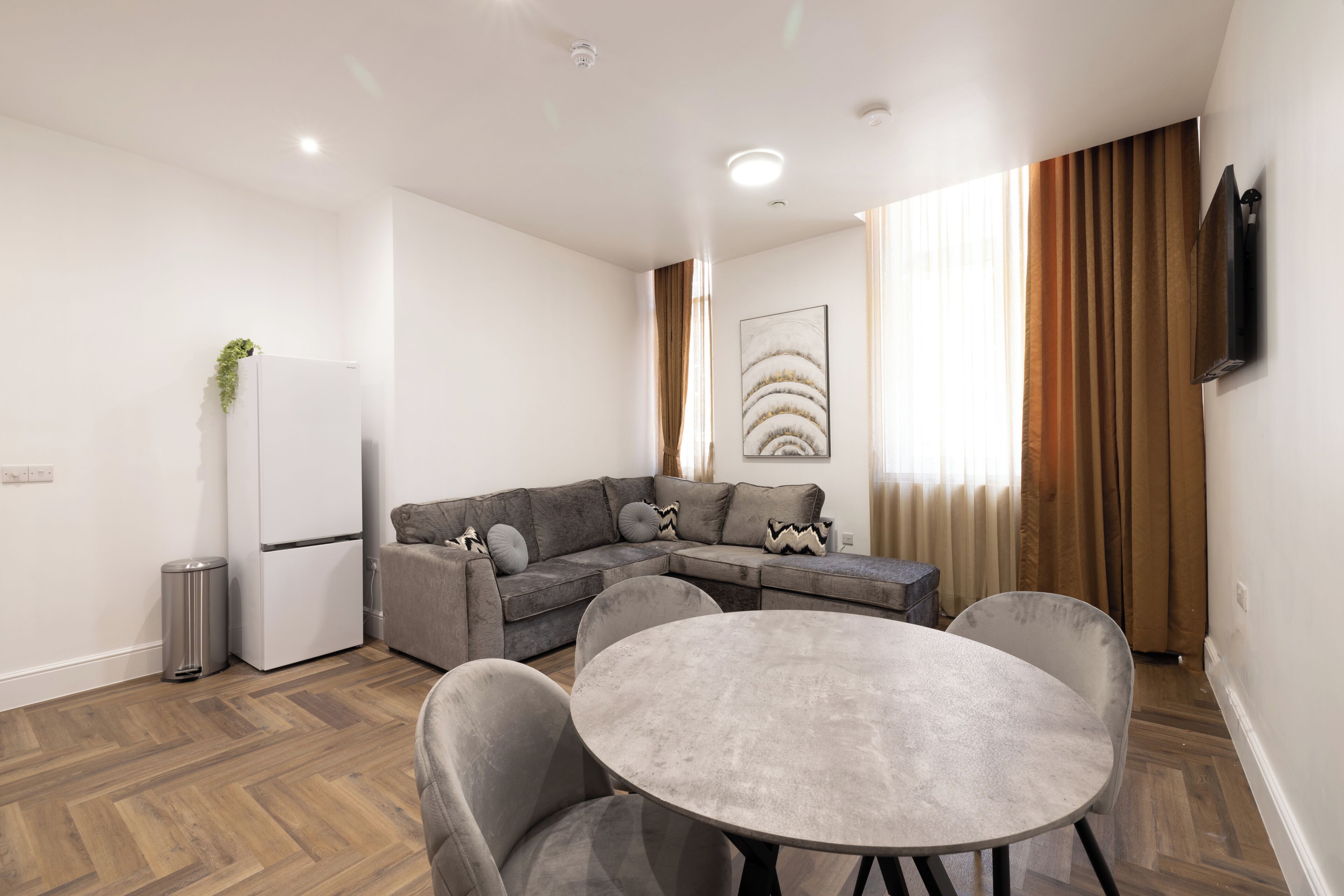A modern living room with a sectional sofa, a round table, and a flat-screen TV mounted on the wall.