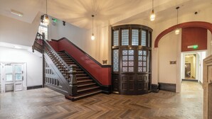 Una imponente escalera con barandilla roja, piso de madera y un amplio arco de entrada con vidrieras.
