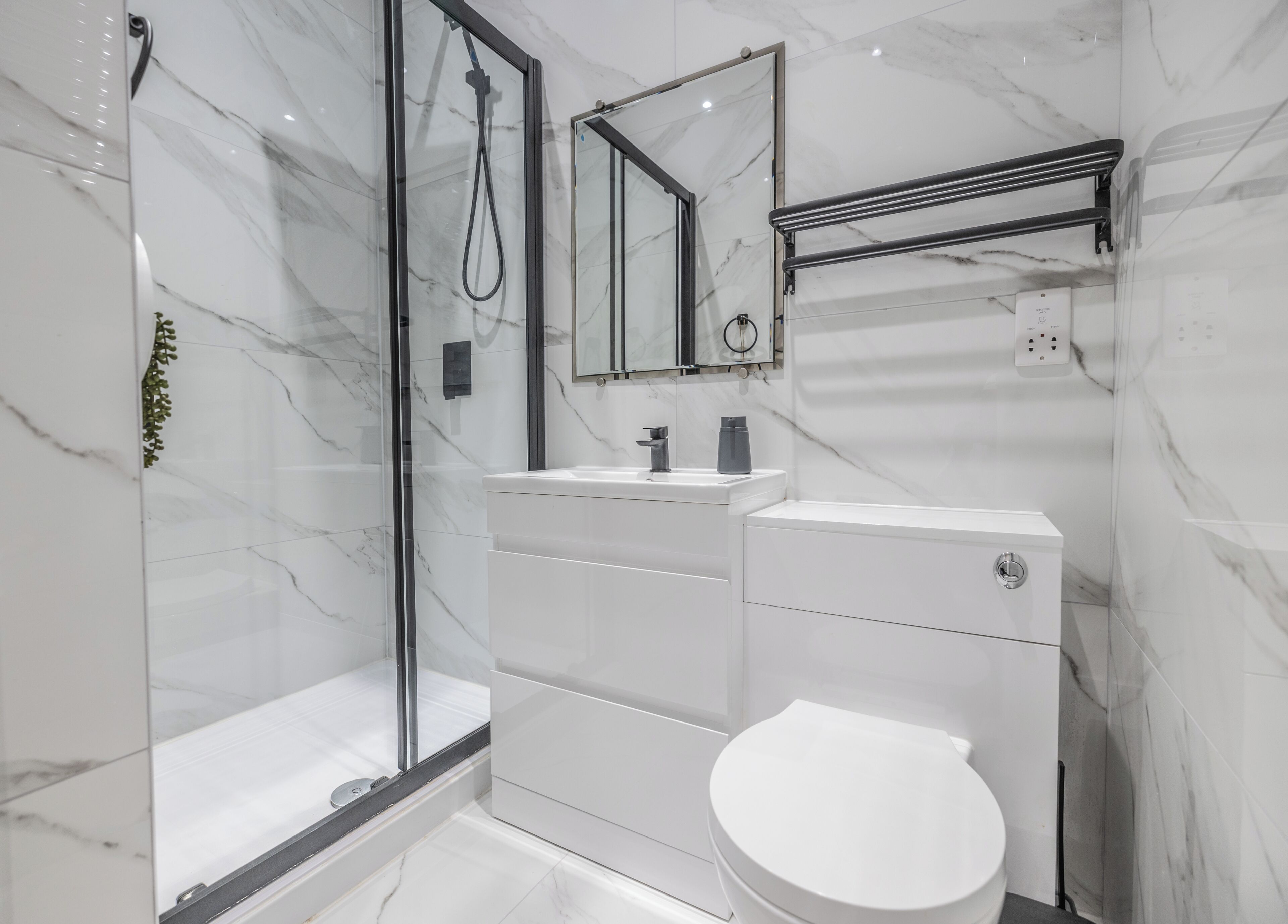 A modern bathroom with a glass shower enclosure, a white toilet, and a vanity with a mirror.