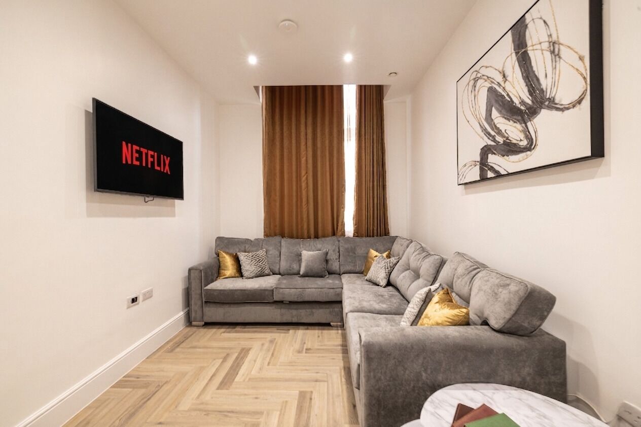 A modern living room with a gray sectional sofa, a mounted TV displaying 'NETFLIX,' and a large abstract painting on the wall.
