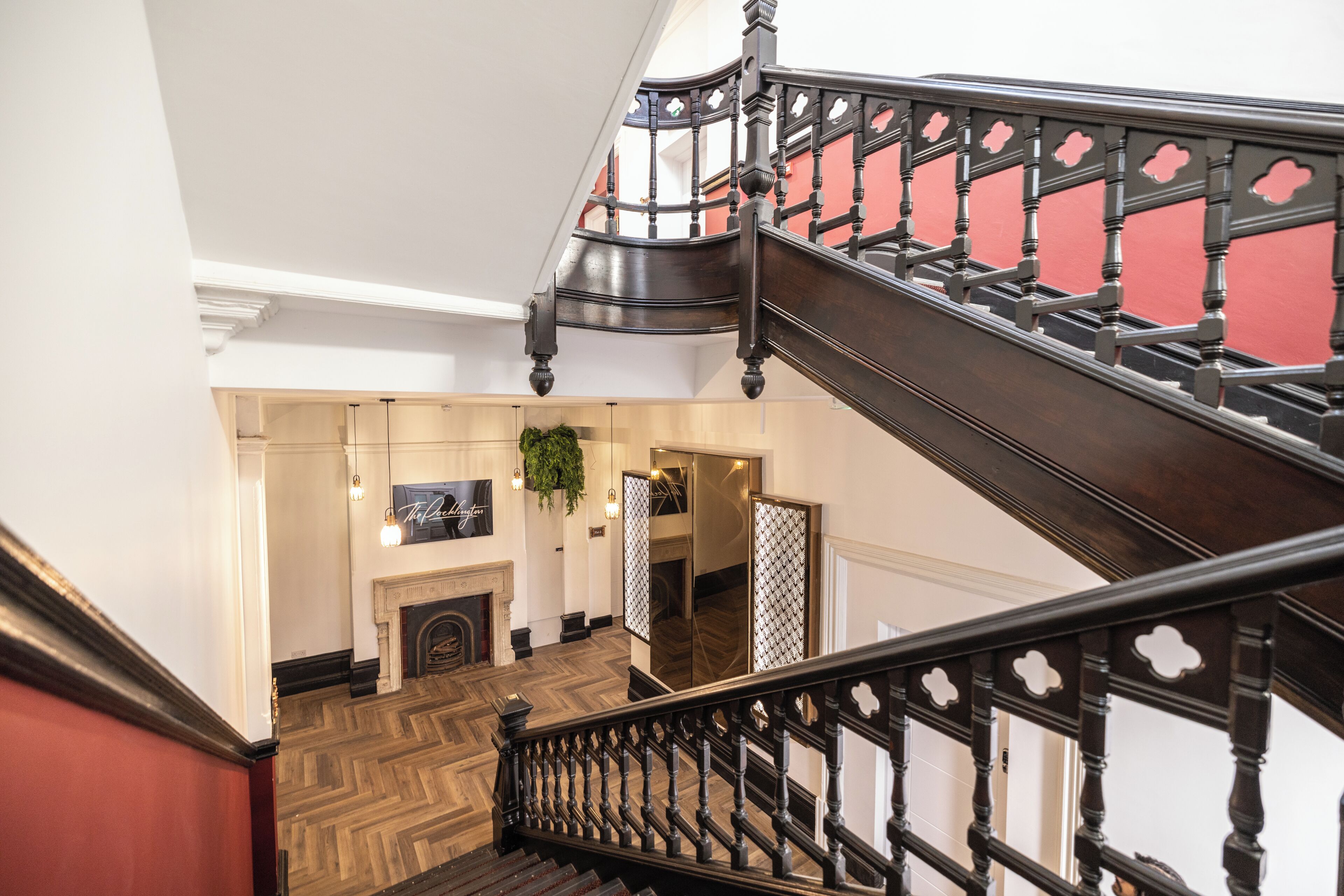 A grand staircase with ornate railings, a wooden floor, and a red accent wall.