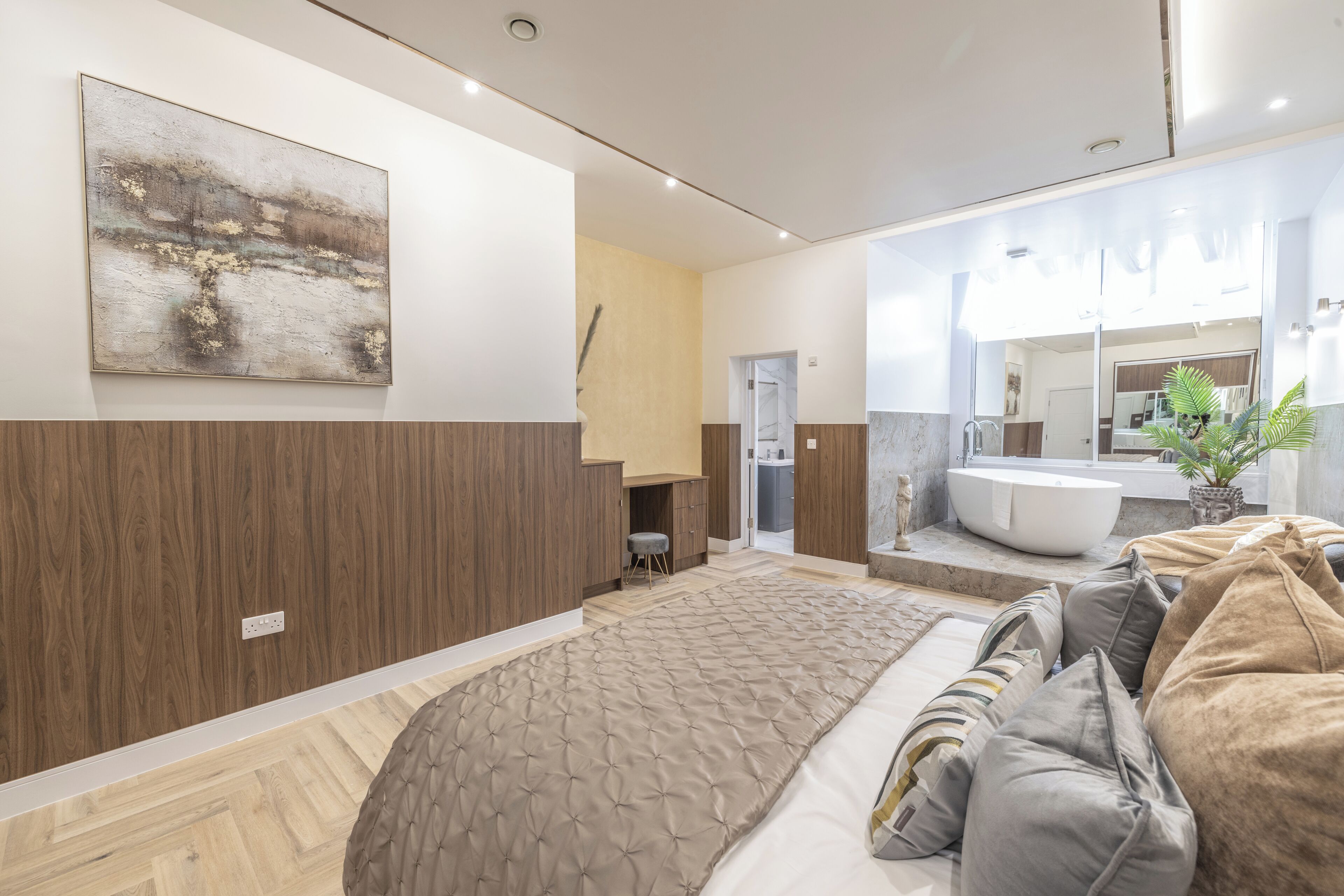 A modern bedroom with a large bed, a desk, a bathroom with a bathtub, and a large window.
