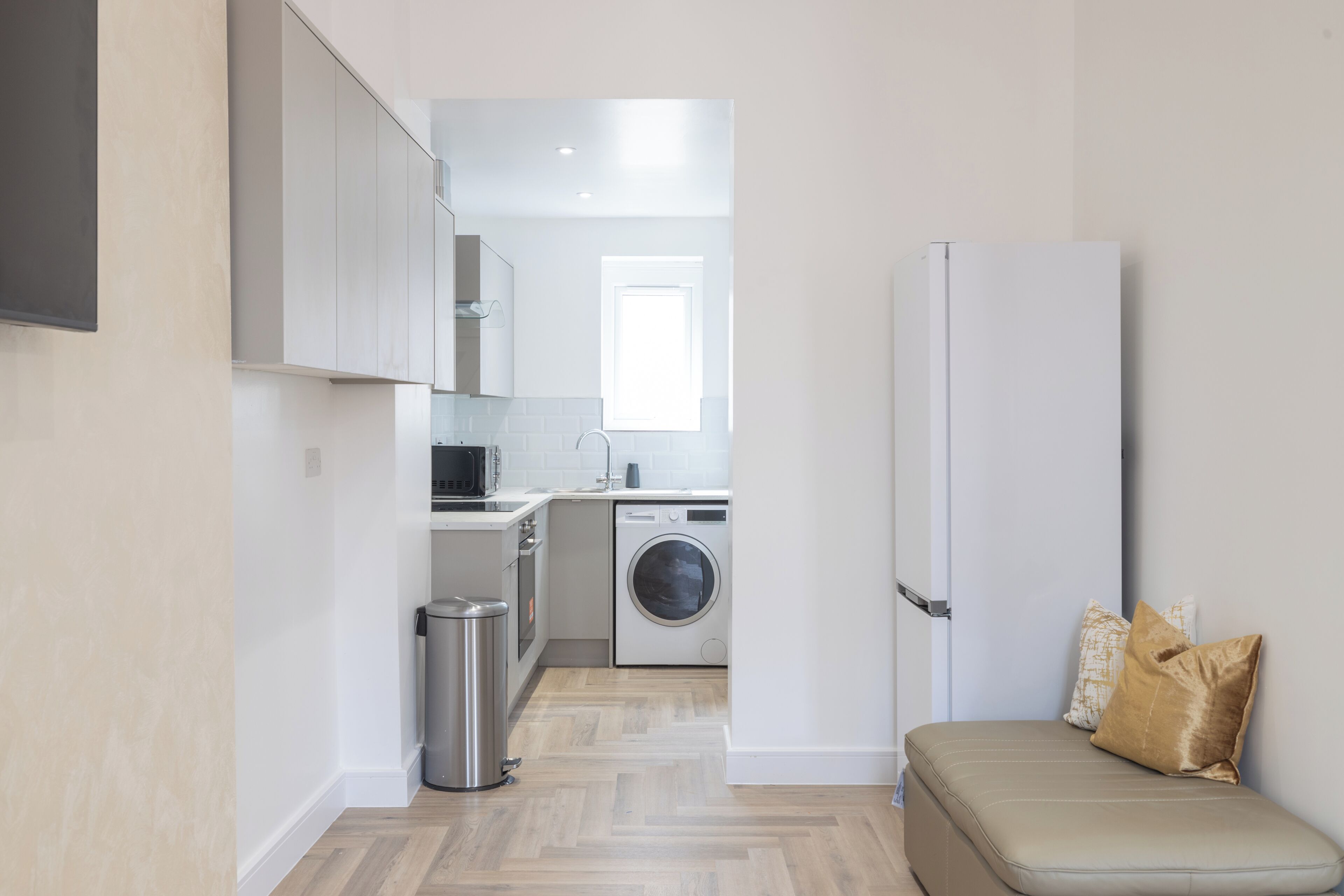 A compact kitchen with a washing machine, a refrigerator, and a bench with cushions.