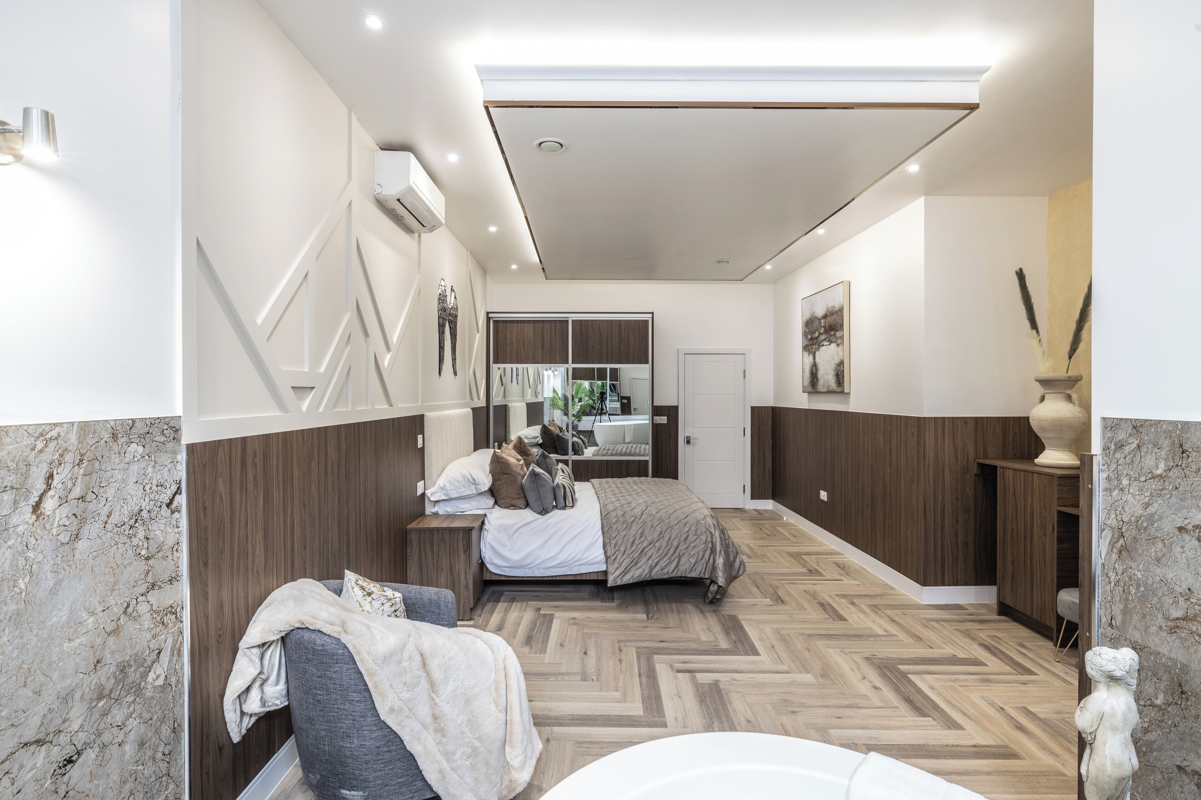 Un dormitorio moderno con cama, mesitas de noche, un espejo y un jarrón decorativo.