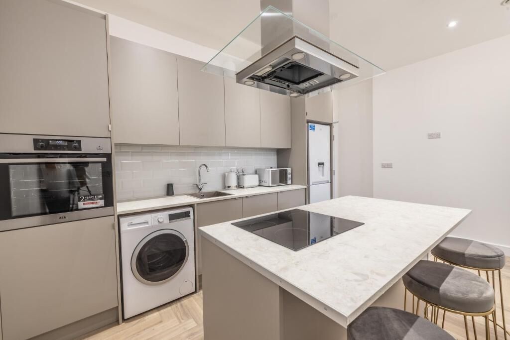 A modern kitchen with a built-in oven, microwave, and dishwasher, a central island with stools, and a glass-fronted range hood.