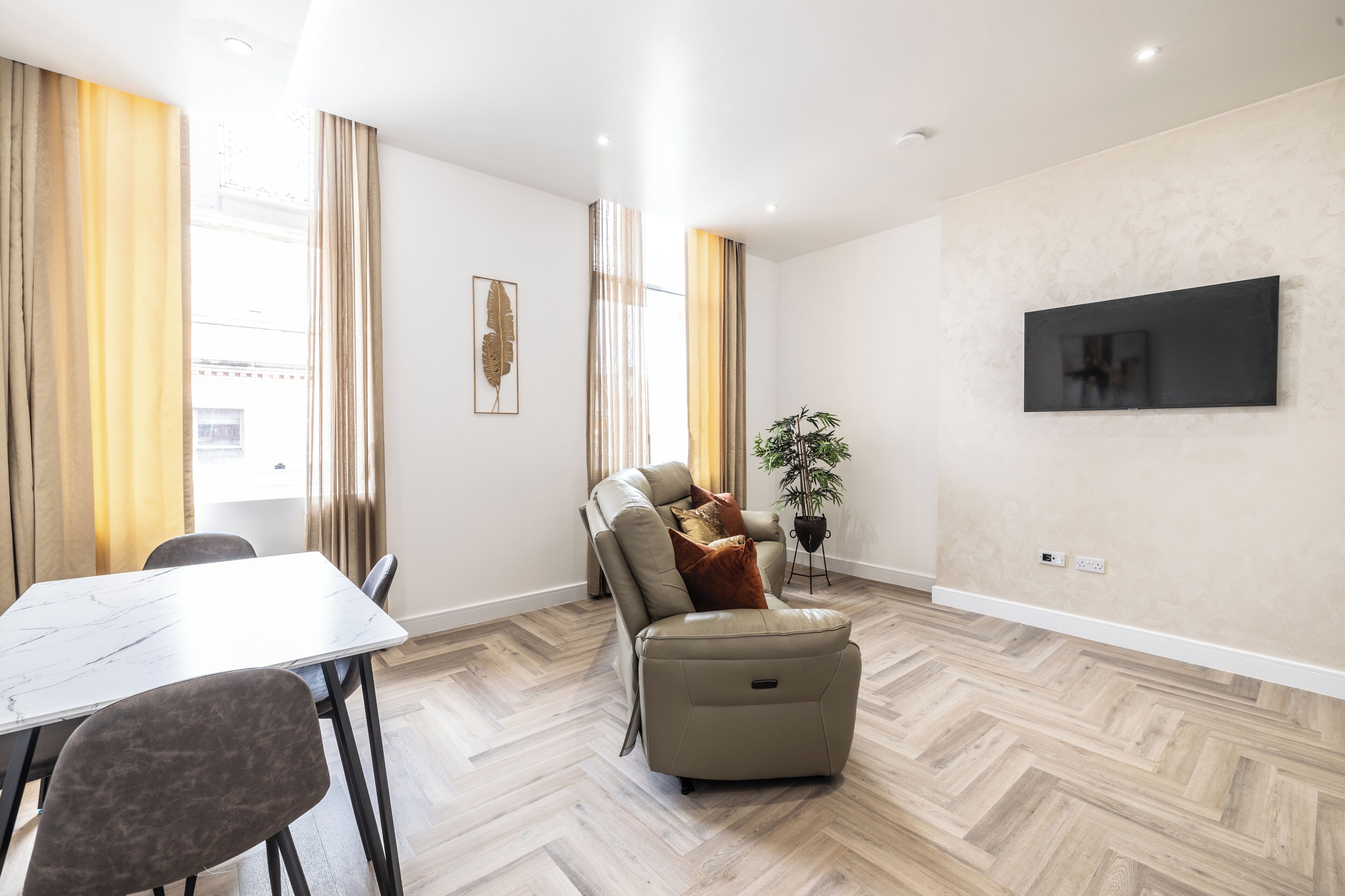Een moderne woonkamer met een bank, een eettafel en een televisie aan de wand.