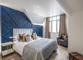 A modern bedroom with a large bed, a side table, a chair, and a window with curtains.