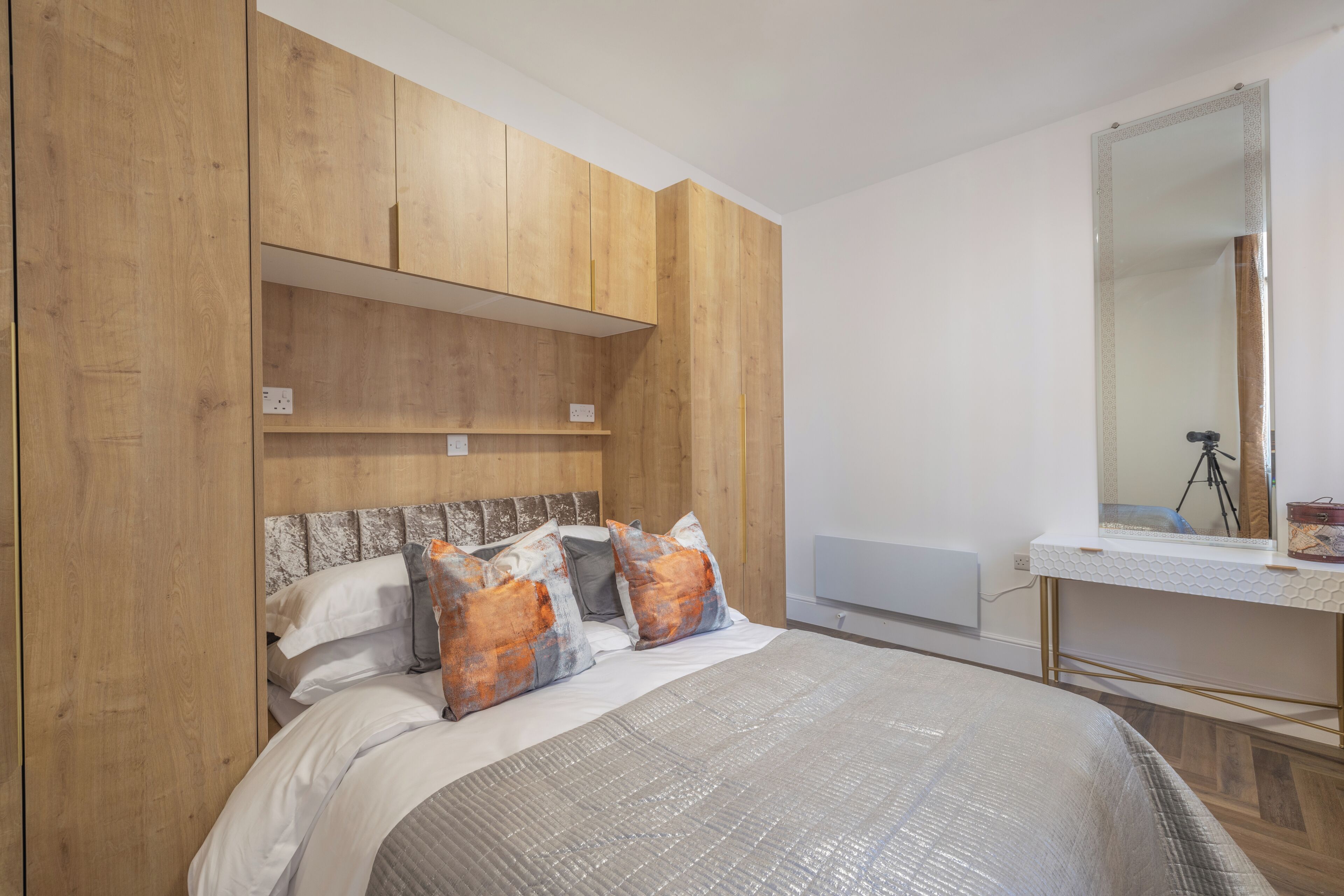 A bedroom with a bed, wooden wardrobe, and a mirror.