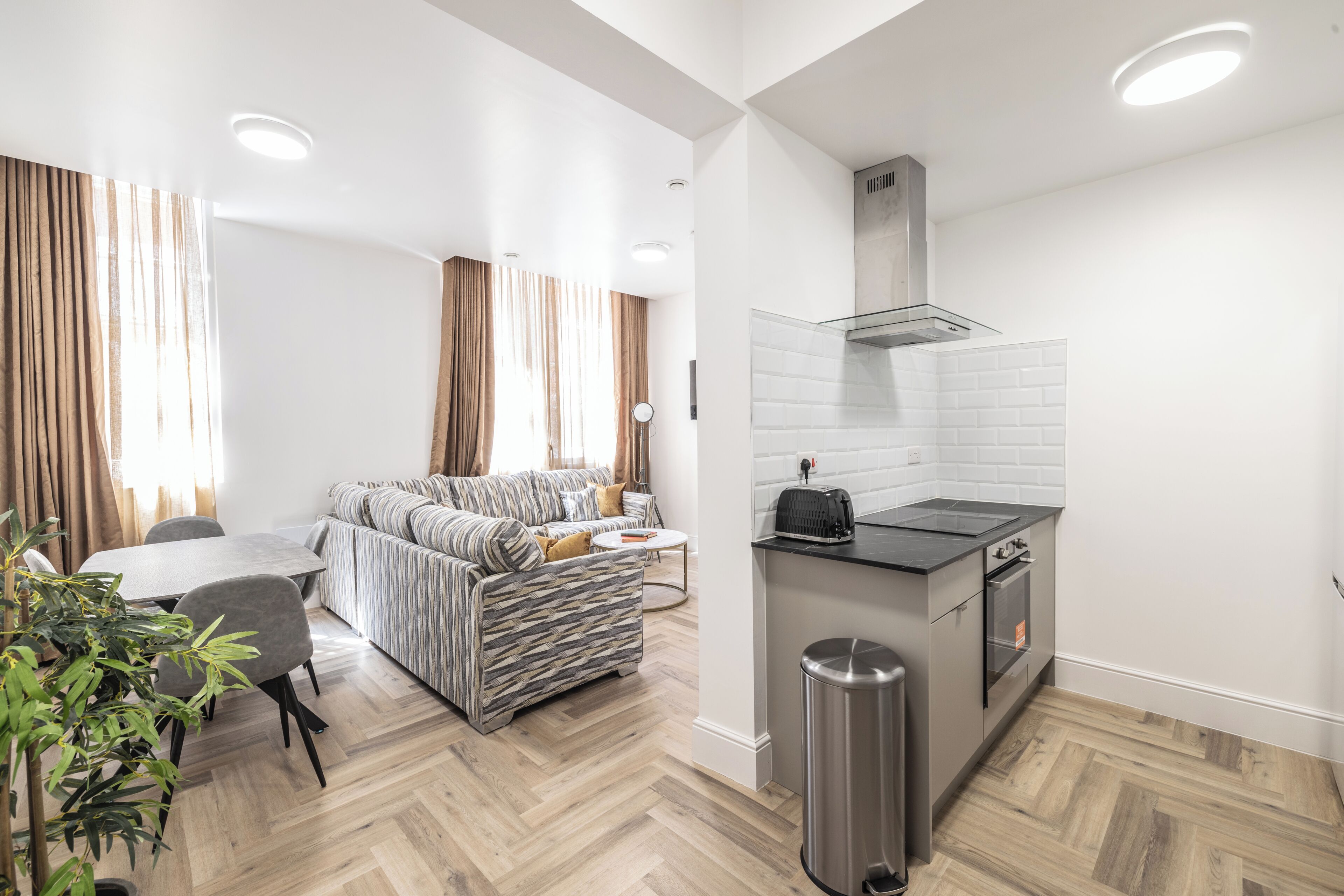 Ein modernes Wohnzimmer mit einer Couch, einem Esstisch und einer Küchenzeile mit Herd und Backofen.