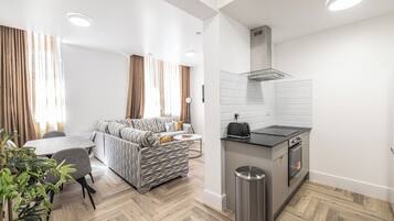 Ein modernes Wohnzimmer mit einer Couch, einem Esstisch und einer Küchenzeile mit Herd und Backofen.