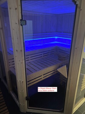 A sauna with a wooden interior and a glass door, featuring a blue light strip along the benches. - Blauer Stein - Vibe - zh2a-haus (Pulheim)